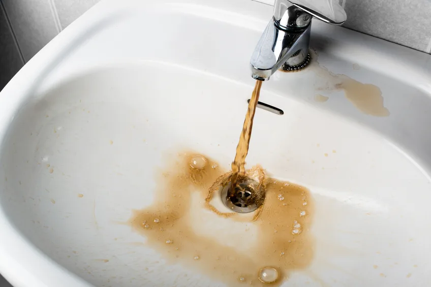 Cloudy, rusty tap water running into a sink